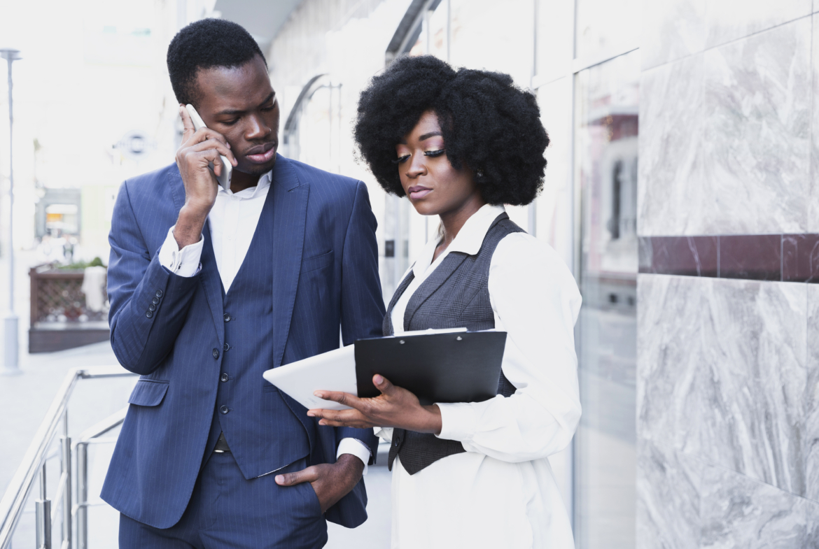 african-young-businessman-talking-mobile-phone-looking-digital-tablet-hold-by-his-colleague